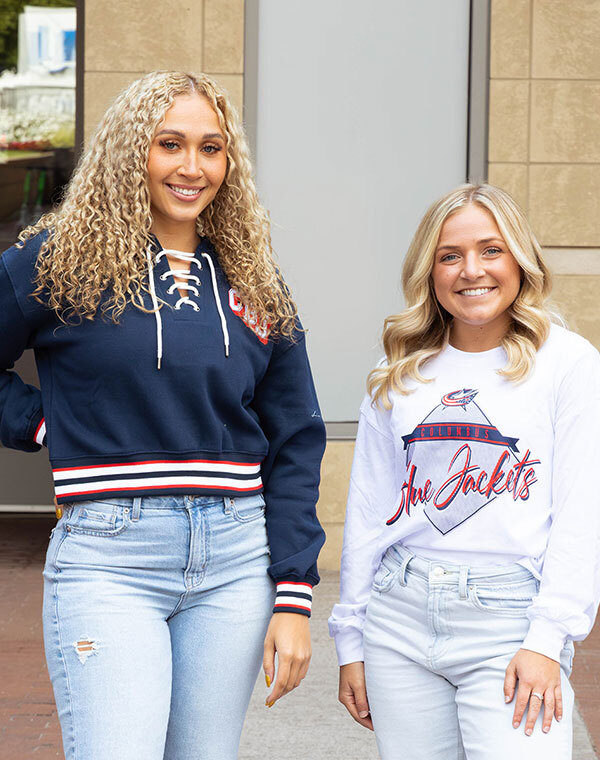 Two women smiling while wearing Columbus Blue Jacket gear