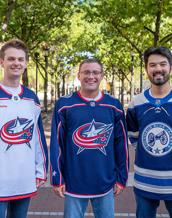 Three men wearing Columbus Blue Jacket Jerseys in front of the arena