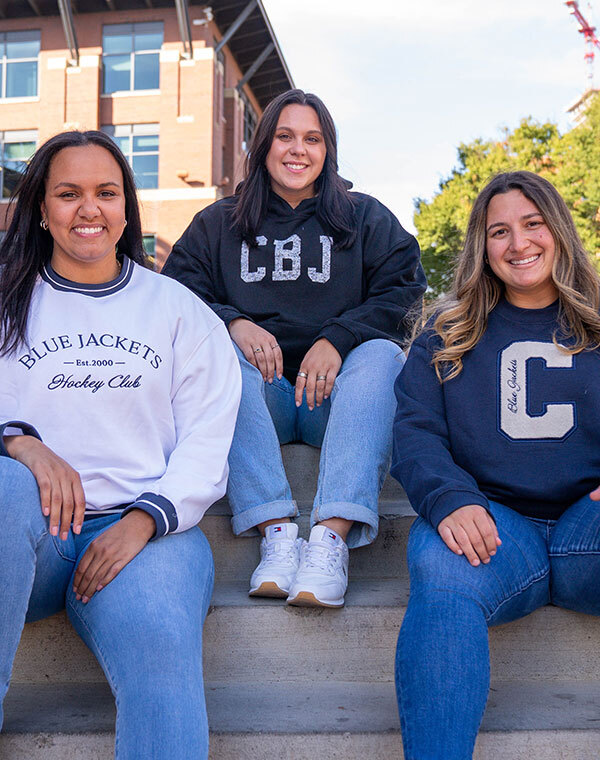 Three women smiling while wearing Columbus Blue Jacket gear