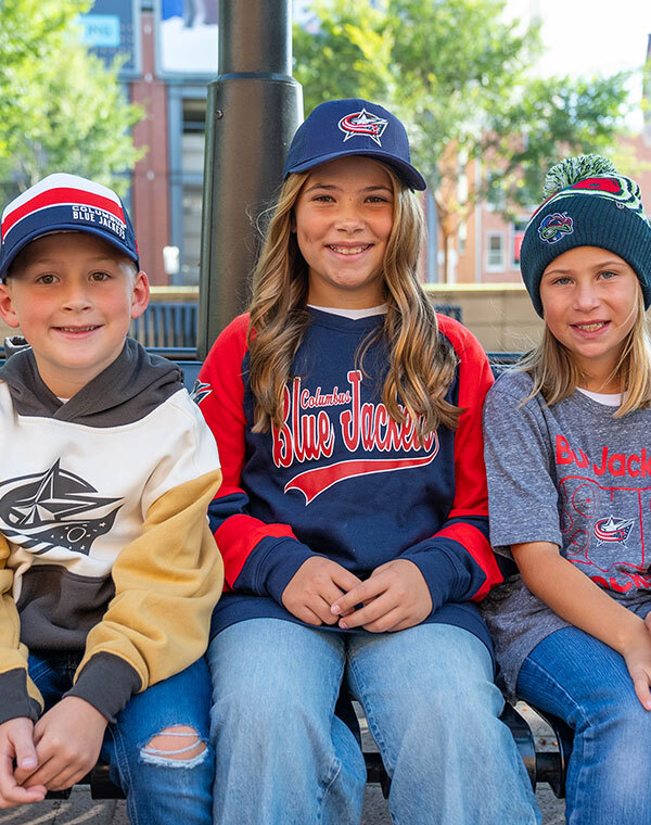 Three children smiling while wearing Columbus Blue Jacket gear