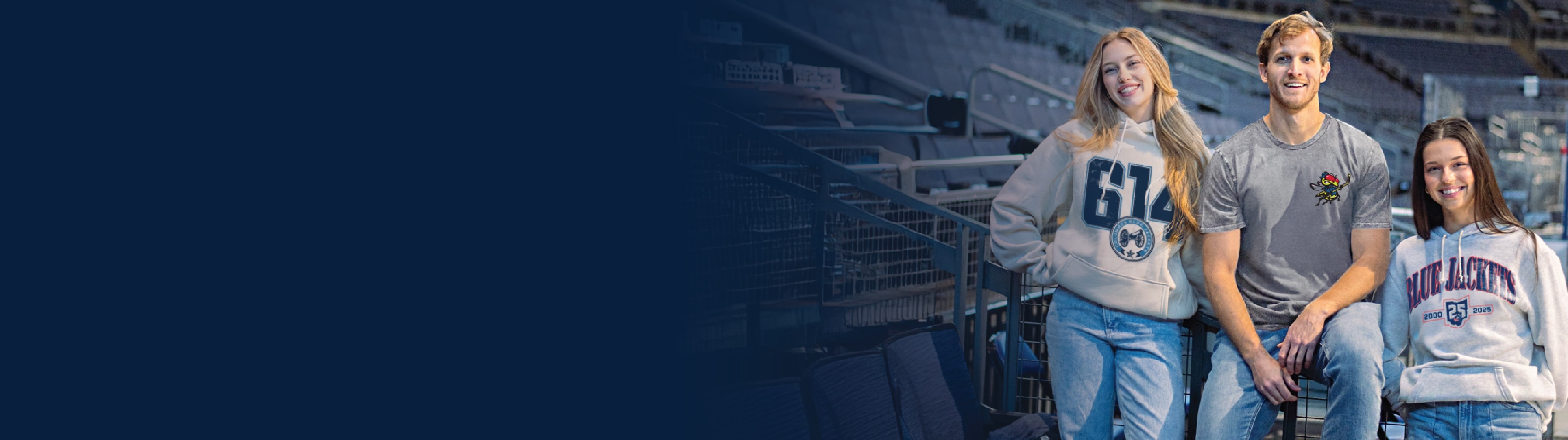Two women and a man smiling while wearing Columbus Blue Jacket merch inside of the arena.